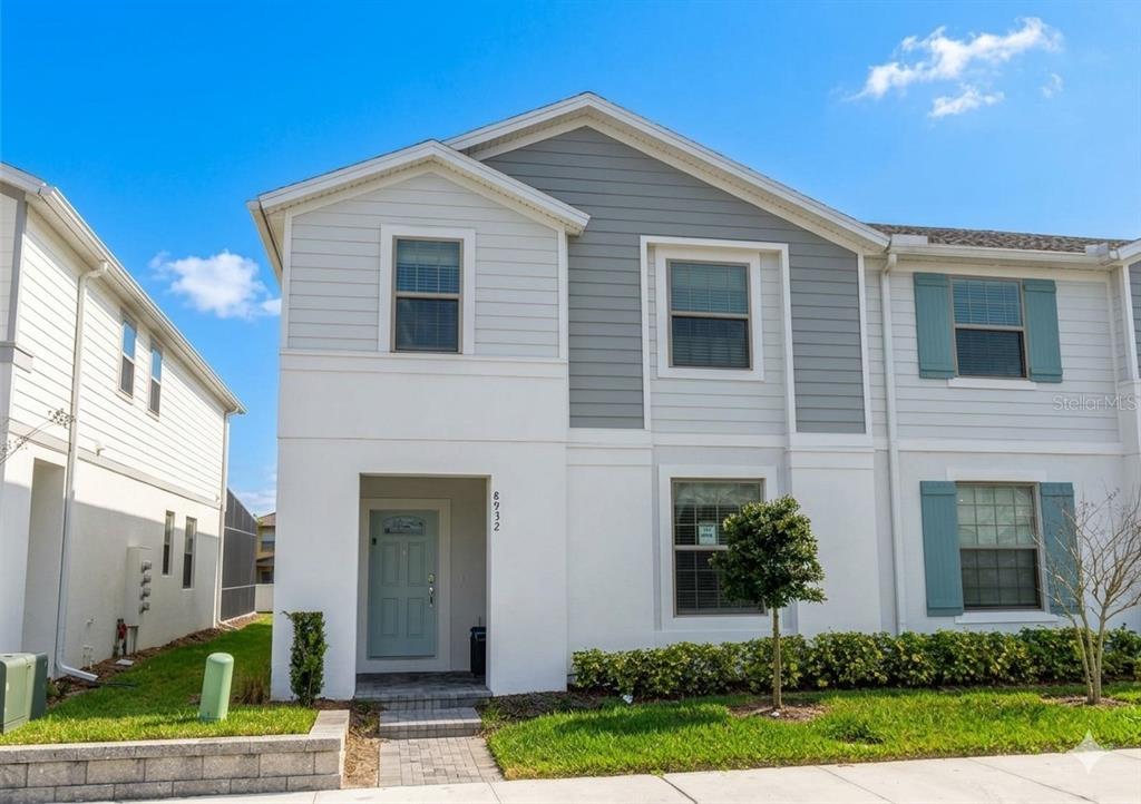A two-story townhouse features white and gray siding, a light blue door, and blue shutters — 8932 SYDNEY AVENUE, KISSIMMEE, FL