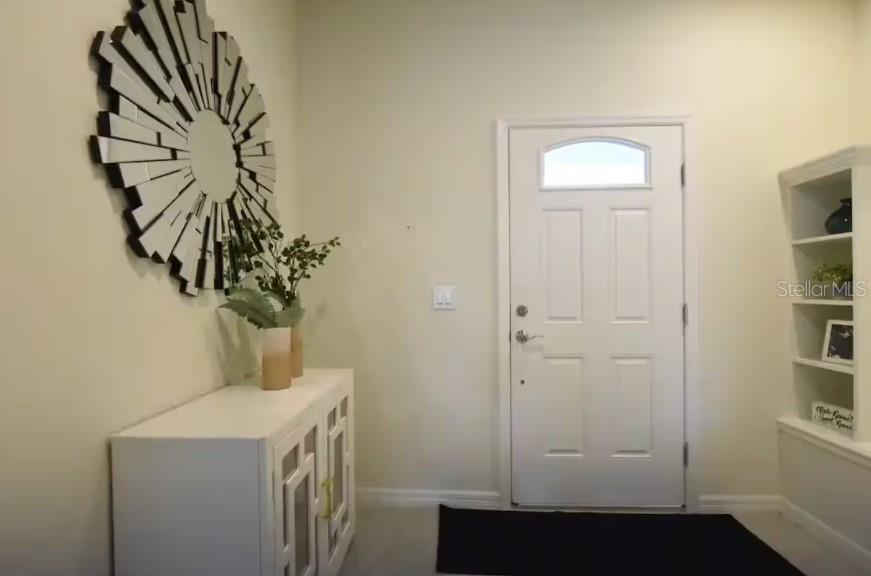 An entryway features a white cabinet, a sunburst mirror, and a white front door — 8932 SYDNEY AVENUE, KISSIMMEE, FL