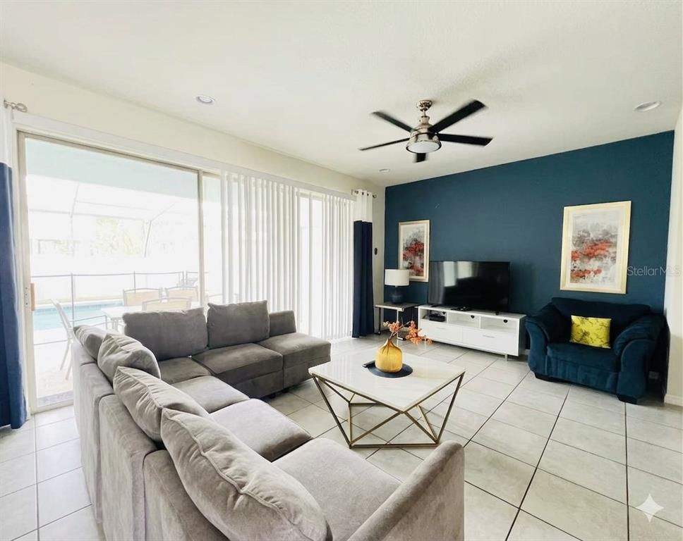 A living room features a blue accent wall, gray sectional sofa, and sliding glass doors — 8932 SYDNEY AVENUE, KISSIMMEE, FL