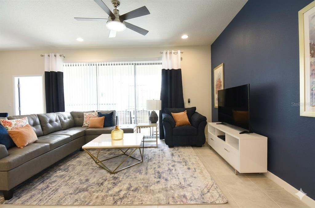 A living room features a gray sectional sofa, a white media console, and navy walls — 8932 SYDNEY AVENUE, KISSIMMEE, FL