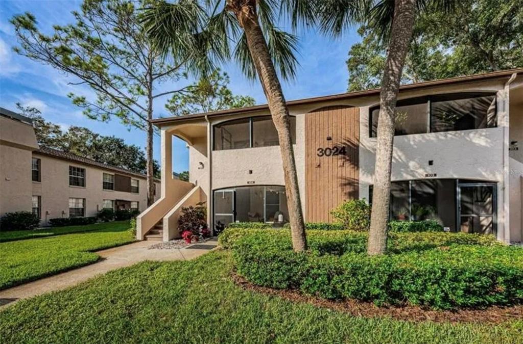 A living room features a stone fireplace, a gray sectional sofa, and wood-look flooring — 3024 BONAVENTURE CIRCLE UNIT 204, PALM HARBOR, FL