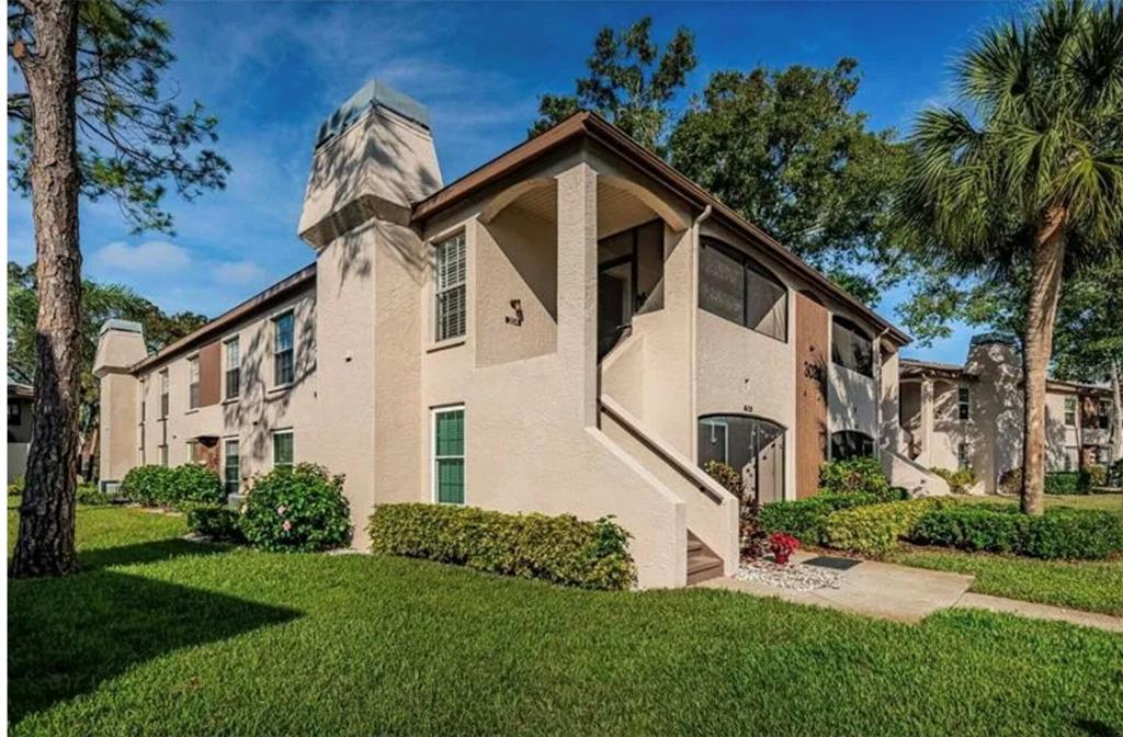 A living room features a stone fireplace, gray sectional sofa, and a ceiling fan — 3024 BONAVENTURE CIRCLE UNIT 204, PALM HARBOR, FL