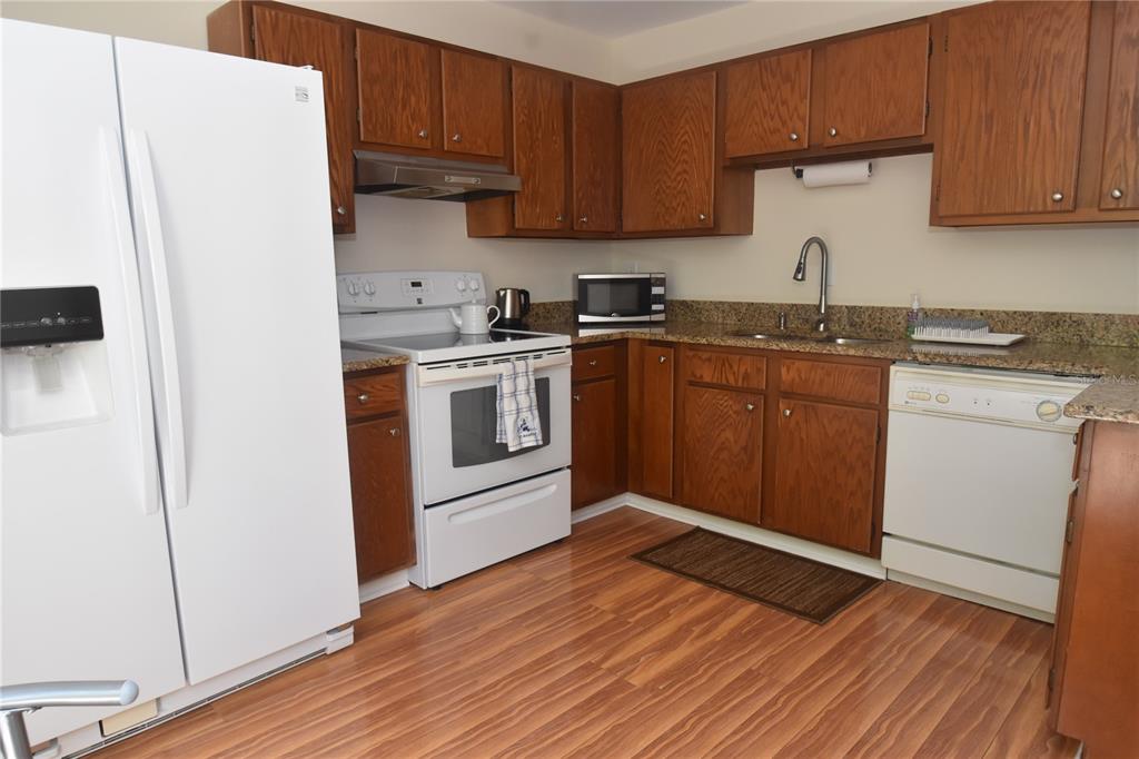 A kitchen features wood cabinets, white appliances, granite countertops, and wood-look flooring — 1677 BROOKHOUSE CIRCLE UNIT BR224, SARASOTA, FL