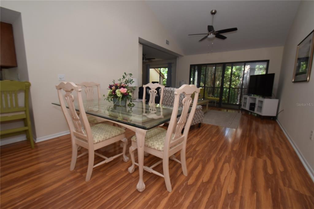 A dining area with a glass table and chairs sits before a living room with flooring — 1677 BROOKHOUSE CIRCLE UNIT BR224, SARASOTA, FL