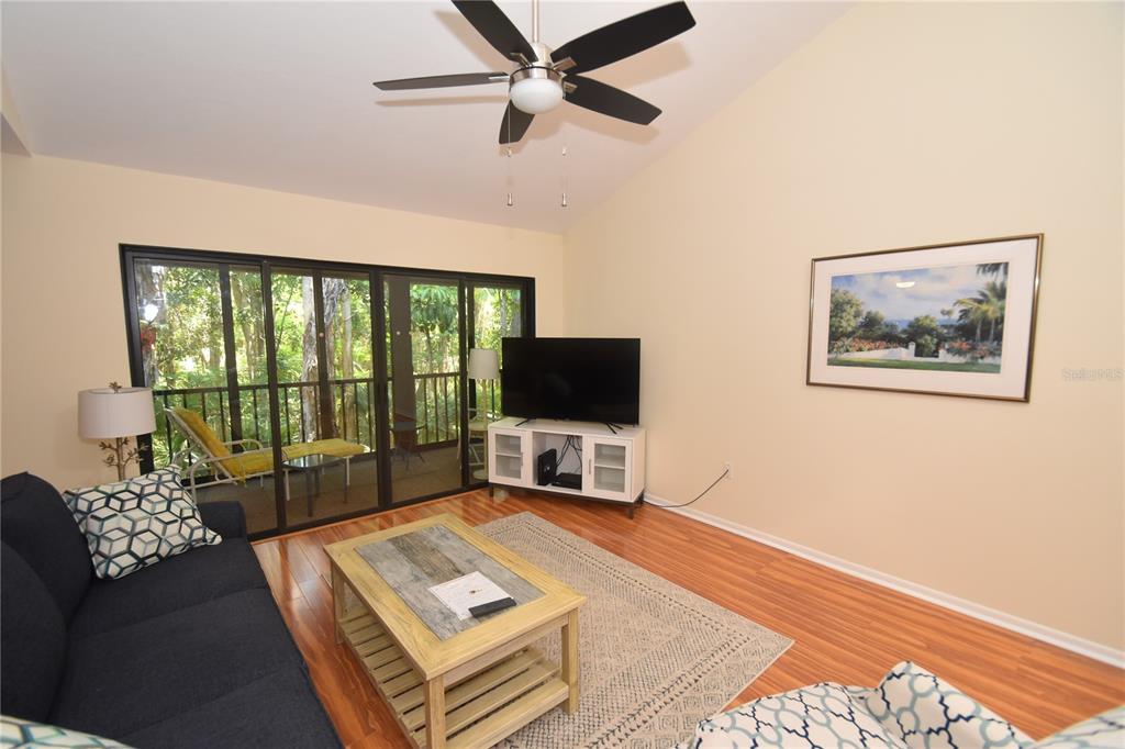 A living room with wood floors, a ceiling fan, a television, and a sliding glass door — 1677 BROOKHOUSE CIRCLE UNIT BR224, SARASOTA, FL
