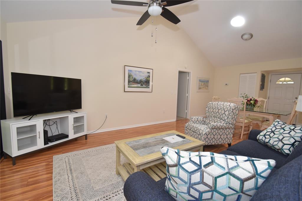 A living room with a vaulted ceiling, wood-look flooring, a television, and a dining area — 1677 BROOKHOUSE CIRCLE UNIT BR224, SARASOTA, FL