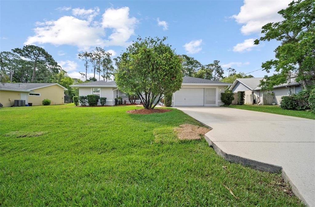 A single-story house with a white garage, a large front tree, and a concrete driveway — 10 FORTRESS PLACE, PALM COAST, FL