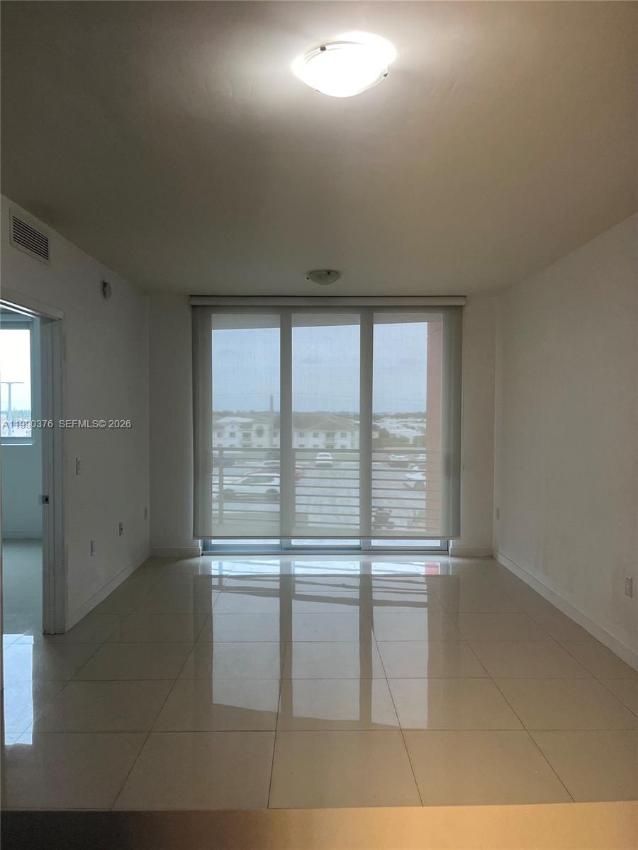 A bright, empty room features white walls, glossy tile flooring, and a large sliding glass door — 7661 NW 107th Ave # 706, Doral FL 33178, DORAL, FL