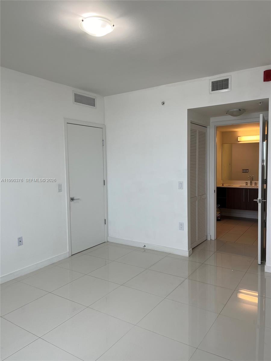 An empty room with white walls, tiled floors, a closed door, and an open bathroom — 7661 NW 107th Ave # 706, Doral FL 33178, DORAL, FL
