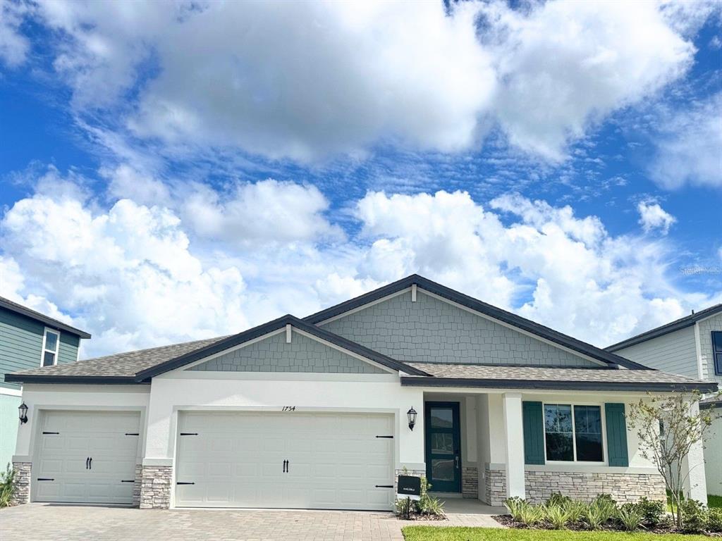 A single-story house exterior features a two-car garage, stone accents, and blue-green shutters — 1754 DRAUGHTON PLACE, ZEPHYRHILLS, FL