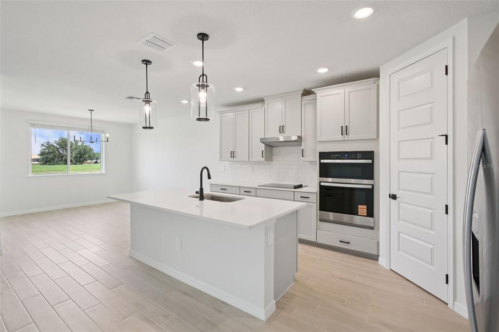 A modern kitchen features light gray cabinets, a white quartz island, and stainless steel appliances — 1754 DRAUGHTON PLACE, ZEPHYRHILLS, FL