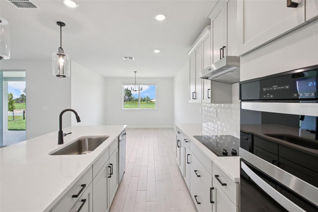 A modern kitchen with white cabinetry, quartz countertops, and stainless steel appliances overlooks a dining area — 1754 DRAUGHTON PLACE, ZEPHYRHILLS, FL