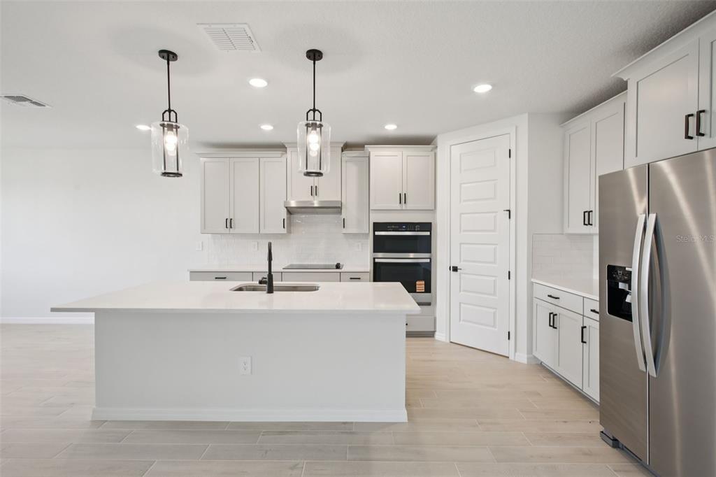 A modern kitchen features white cabinetry, a large central island, stainless steel appliances, and pendant lighting — 1754 DRAUGHTON PLACE, ZEPHYRHILLS, FL