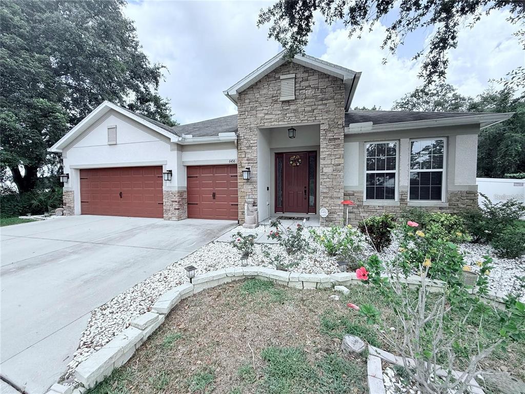 A single-story house with a stone facade, red garage doors, and a landscaped front yard — 6456 DOE PATH COURT, WESLEY CHAPEL, FL