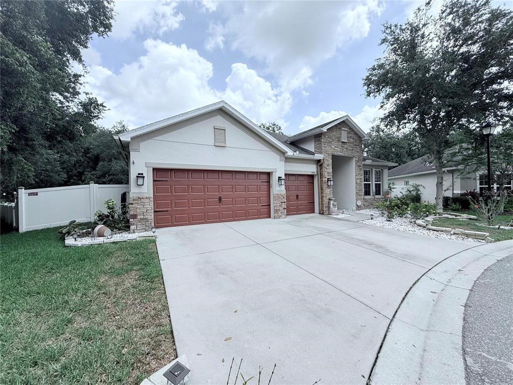 A single-story house with a three-car garage, stone accents, and a concrete driveway — 6456 DOE PATH COURT, WESLEY CHAPEL, FL