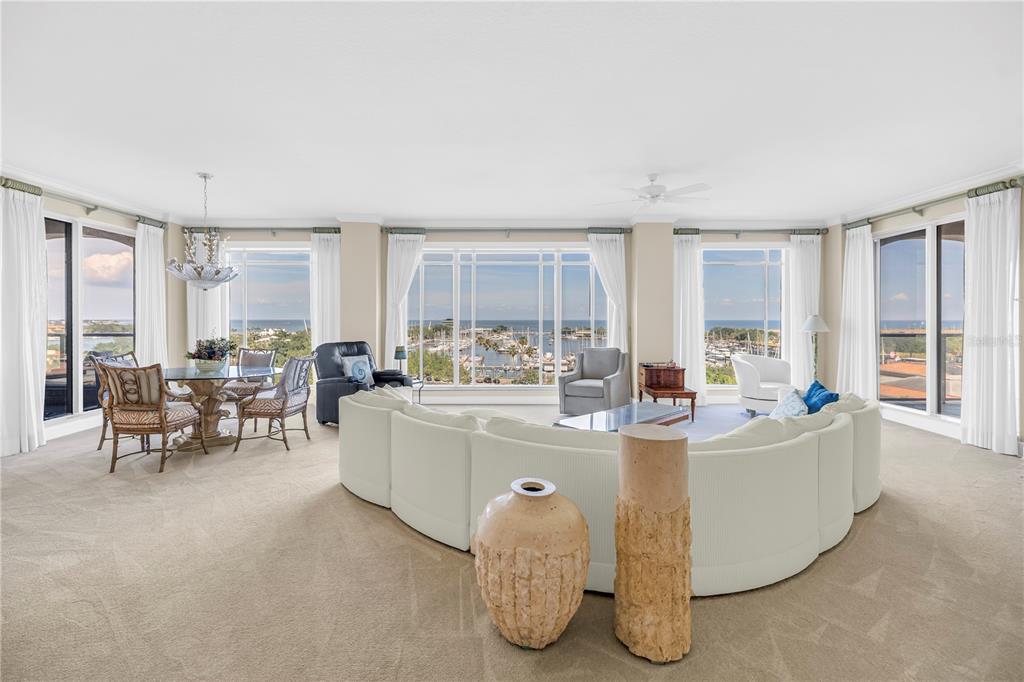A spacious living and dining area features a large curved sofa, floor-to-ceiling windows, and water views — 100 BEACH DRIVE NE UNIT 702, ST PETERSBURG, FL