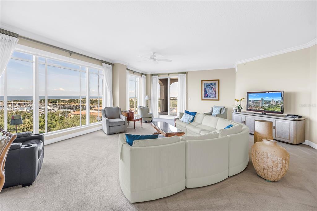 A spacious living room features a curved sectional sofa, large windows, and a marina view — 100 BEACH DRIVE NE UNIT 702, ST PETERSBURG, FL