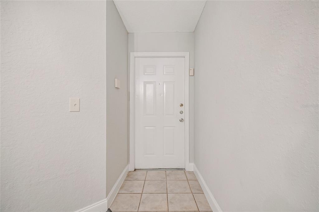 A white front door sits at the end of a small tiled entryway — 7511 SEURAT STREET UNIT 10102, ORLANDO, FL