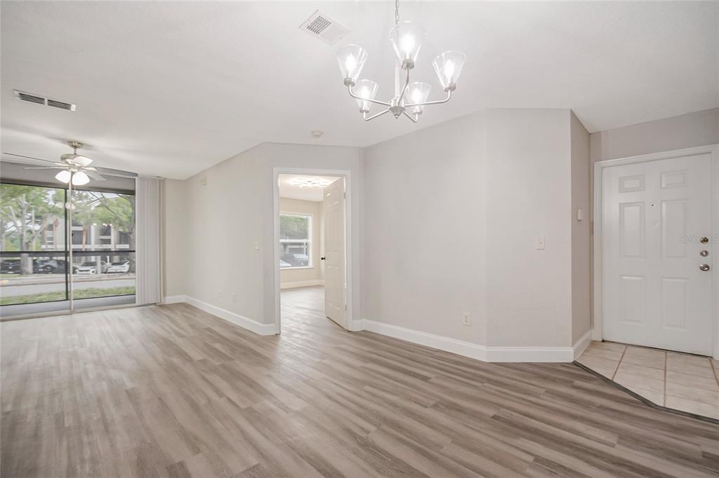 An open living area features light wood-look flooring, a chandelier, and a white front door — 7511 SEURAT STREET UNIT 10102, ORLANDO, FL