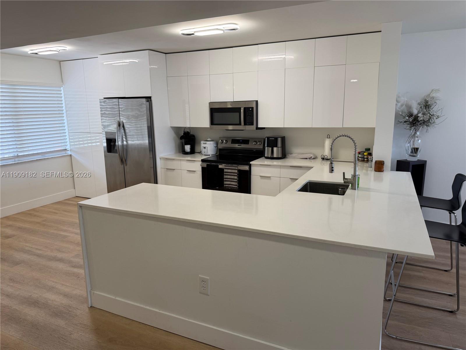 A modern kitchen features white flat-panel cabinetry, stainless steel appliances, and a white quartz peninsula — 2560 NW 103rd Ave # 402, Sunrise FL 33322, SUNRISE, FL