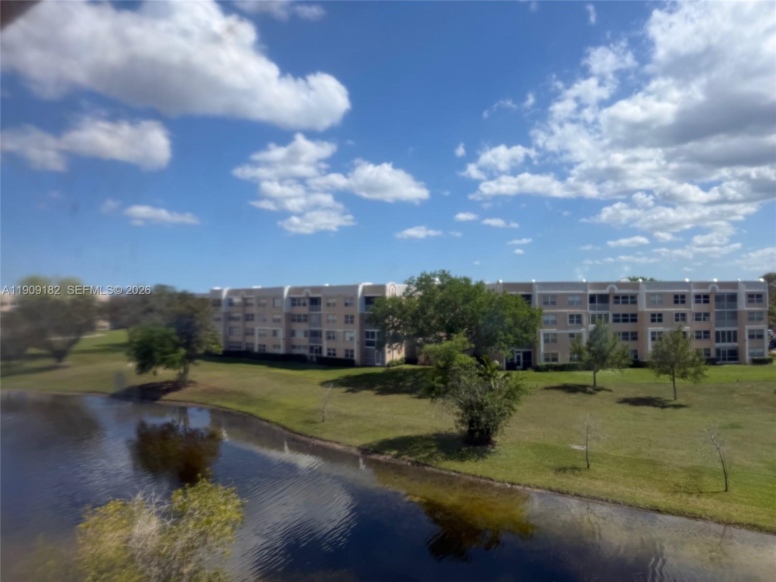 A view of a multi-story apartment building across a small lake and grassy lawn — 2560 NW 103rd Ave # 402, Sunrise FL 33322, SUNRISE, FL