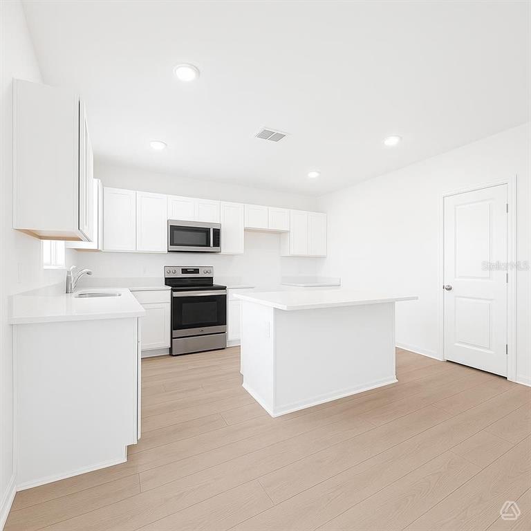 A modern kitchen features white cabinetry, stainless steel appliances, a center island, and light flooring — 12926 RED DEER PLACE, PARRISH, FL