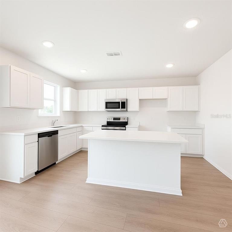 A bright kitchen features white cabinets, a central island, stainless steel appliances, and wood-look flooring — 12926 RED DEER PLACE, PARRISH, FL