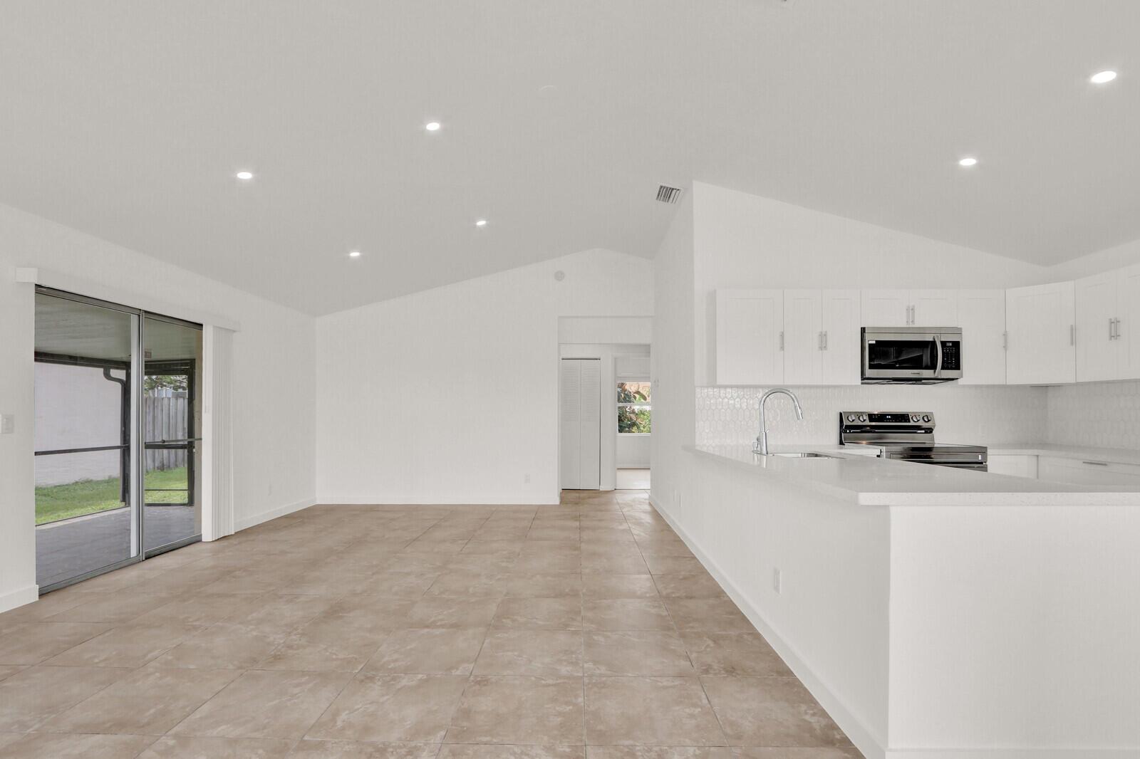 A bright, open-concept living area with tile flooring, recessed lighting, and an adjacent white kitchen — 152 Wandering Trail, Jupiter FL 33458, JUPITER, FL