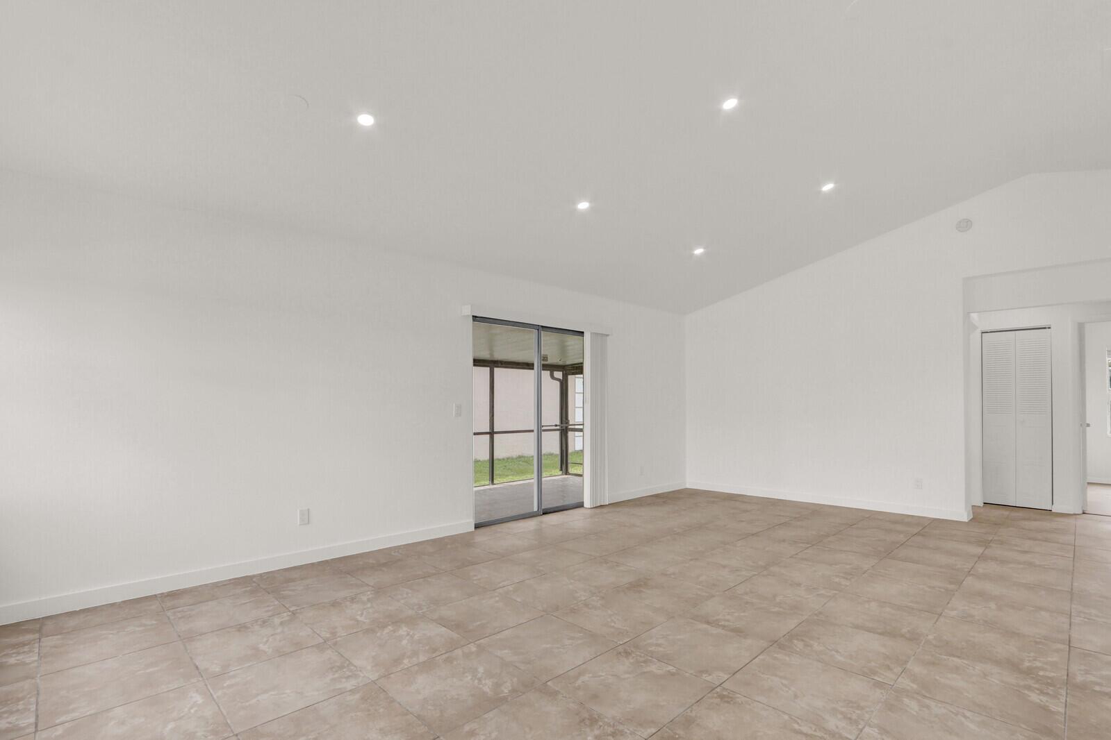 An empty room features white walls, recessed lighting, tile flooring, and a sliding glass door — 152 Wandering Trail, Jupiter FL 33458, JUPITER, FL