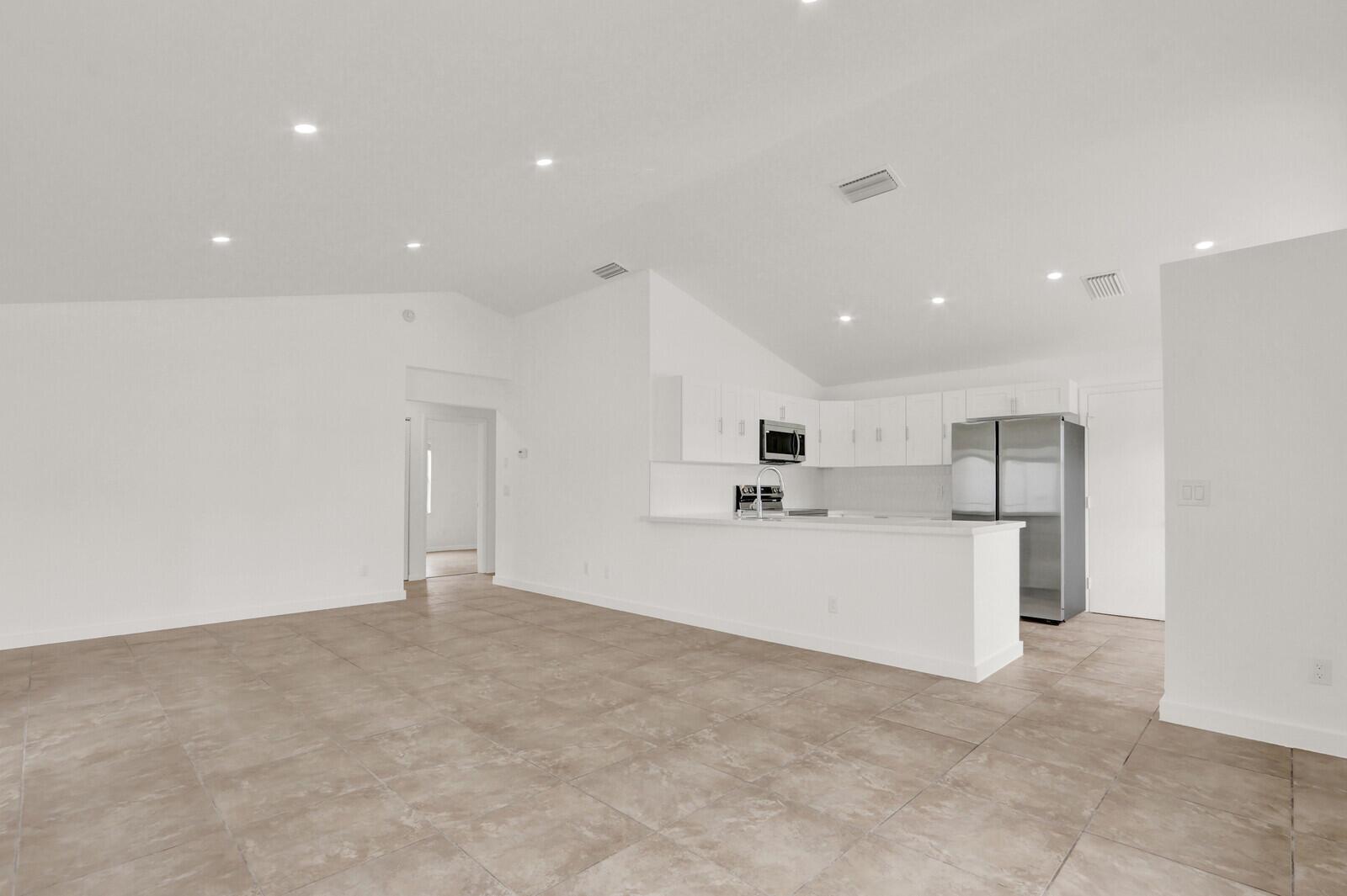 An open-concept kitchen and living area with white cabinets, stainless steel appliances, and tile flooring — 152 Wandering Trail, Jupiter FL 33458, JUPITER, FL