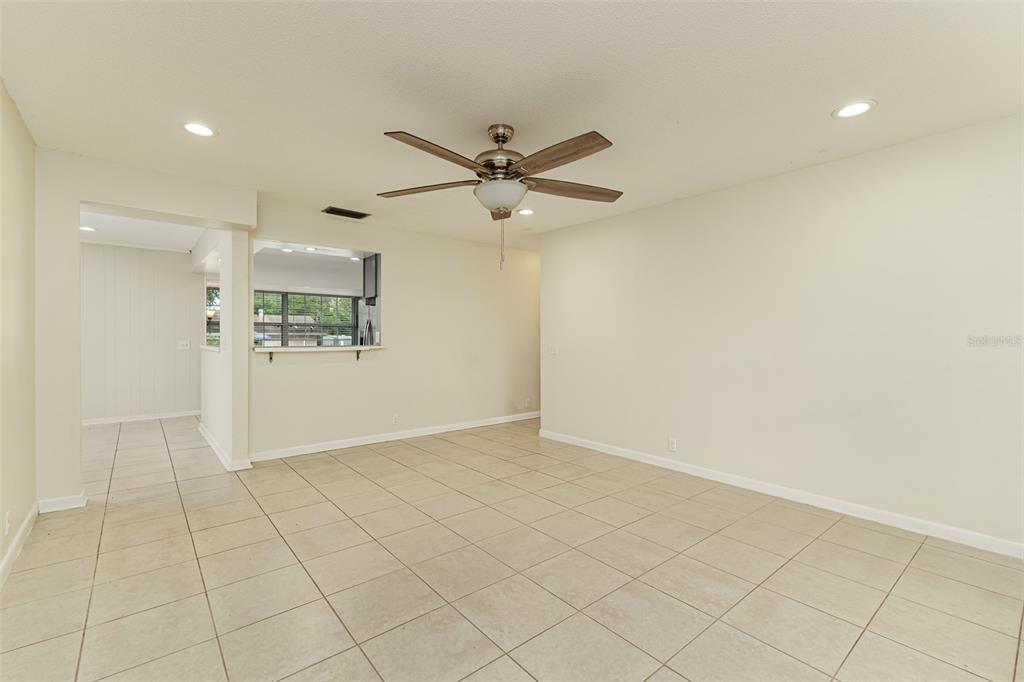 An empty room with beige tile flooring, a ceiling fan, and a kitchen pass-through window — 408 LAKE NED, WINTER HAVEN, FL