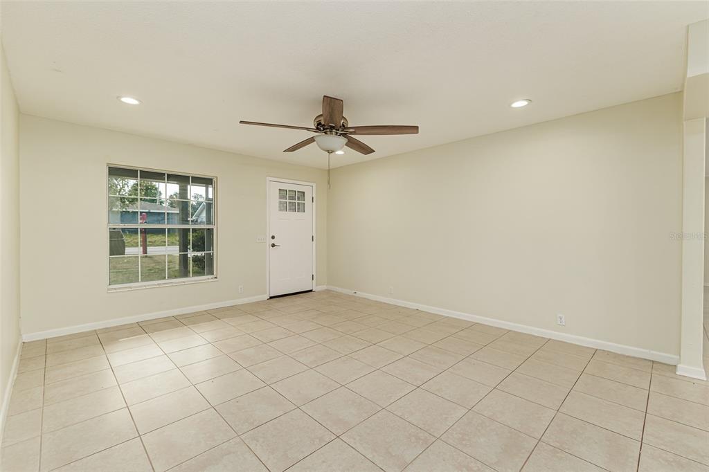 An empty room with beige tile flooring, a ceiling fan, and a white front door — 408 LAKE NED, WINTER HAVEN, FL