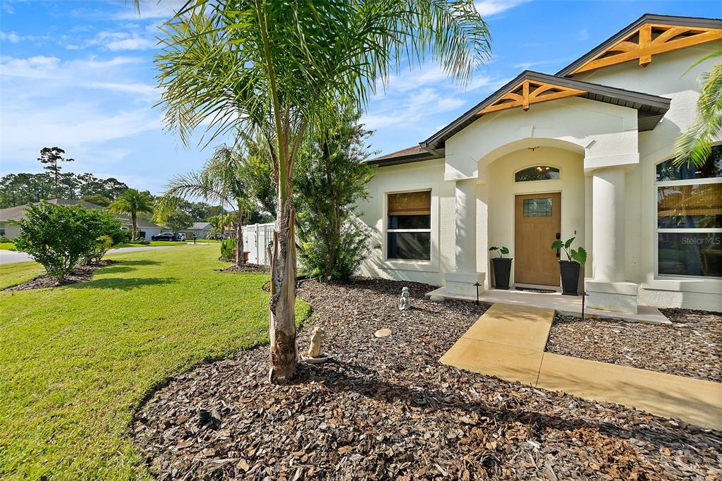 The exterior of a light-colored house features a palm tree, mulch landscaping, and a walkway — 20 EASTWOOD DRIVE, PALM COAST, FL