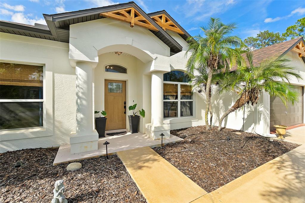 The exterior of a house features a covered entryway, a wooden door, and palm trees — 20 EASTWOOD DRIVE, PALM COAST, FL