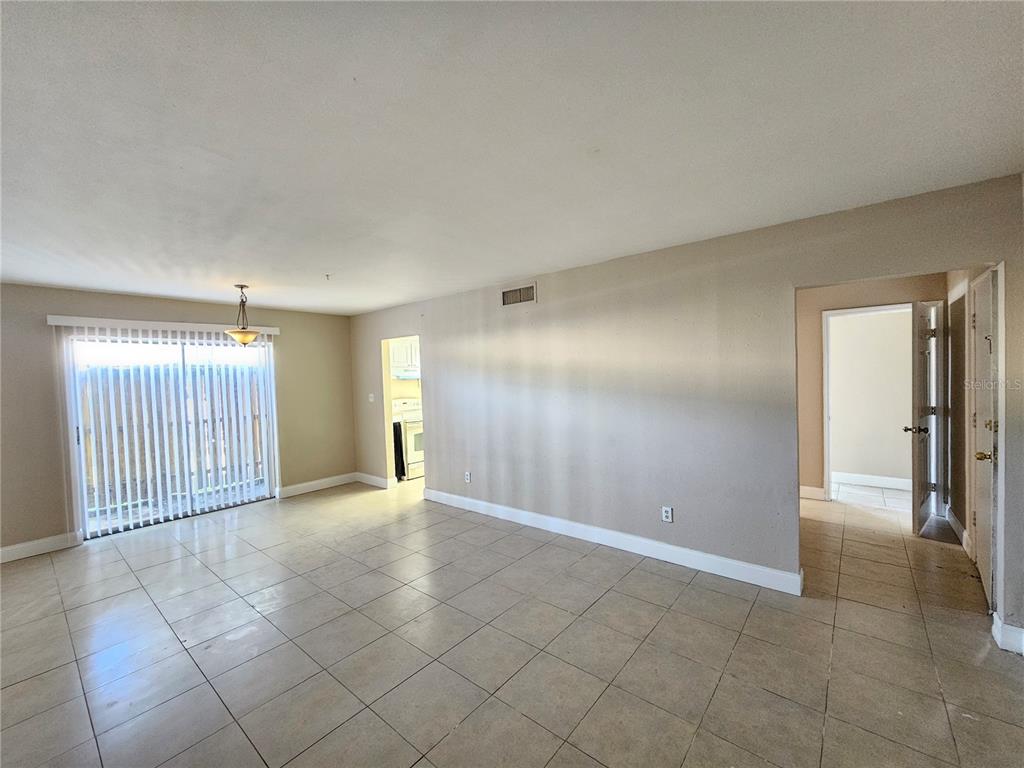 An empty living room features beige tile flooring, a sliding glass door, and neutral walls — 7602 POWHATAN AVENUE W UNIT 3, TAMPA, FL