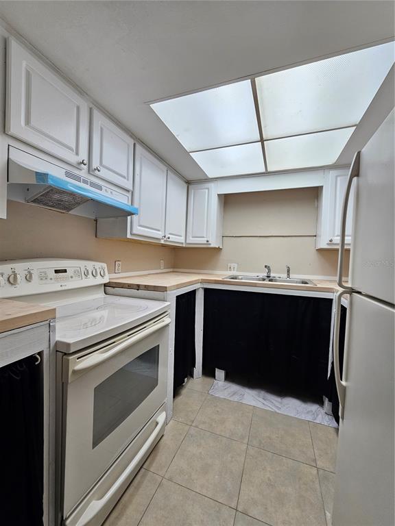 A kitchen features white cabinets, a butcher block countertop, a stove, and black fabric curtains — 7602 POWHATAN AVENUE W UNIT 3, TAMPA, FL