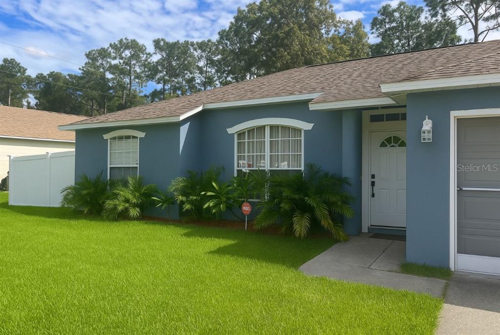 A blue house exterior features a white front door, a garage, and small palm bushes — 1293 COURTLAND BOULEVARD, DELTONA, FL