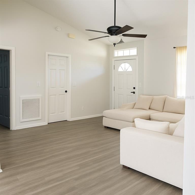 A living room features light wood-look flooring, white walls, a ceiling fan, and cream-colored sofas — 1293 COURTLAND BOULEVARD, DELTONA, FL