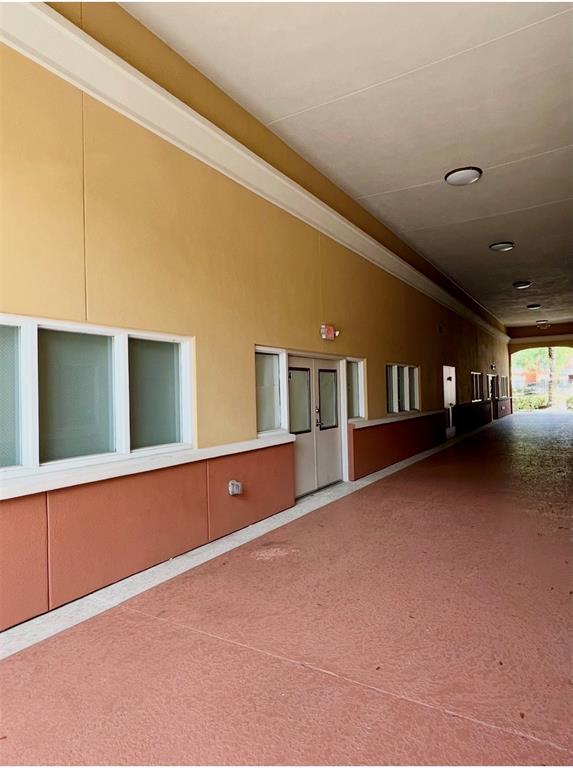 A covered outdoor walkway runs along the side of a building with tan and red walls — 8751 COMMODITY CIRCLE UNIT 4, ORLANDO, FL