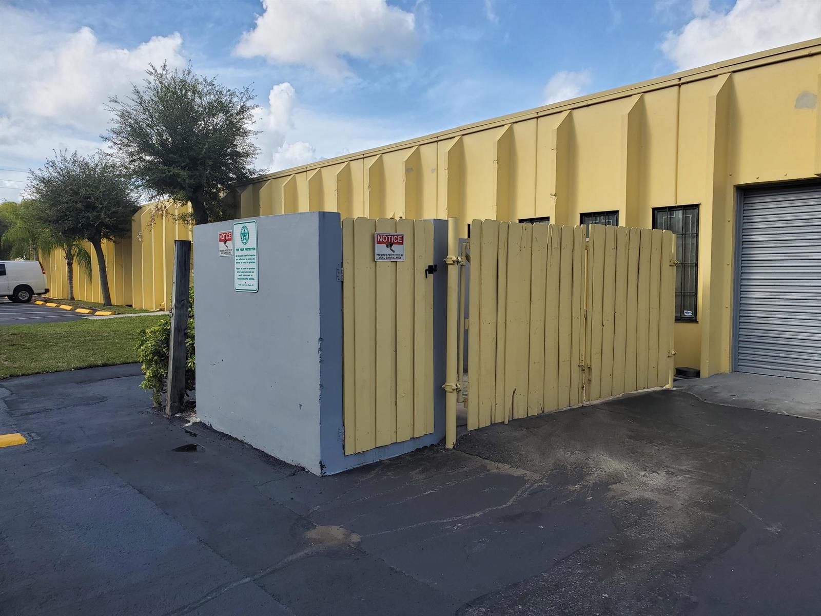 A gray concrete enclosure with a yellow wooden gate stands beside a yellow industrial building — 2501 NW 17th Lane # B, Pompano Beach FL 33064, POMPANO BEACH, FL