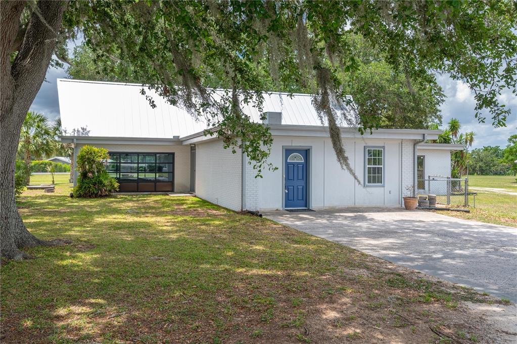 A white brick house with a metal roof, blue front door, and a glass garage door — 1325 THORNBURG ROAD, BABSON PARK, FL