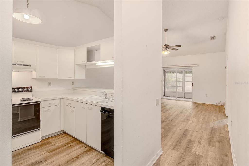 A kitchen with white cabinets and appliances opens into a living area with wood flooring — 39650 US HIGHWAY 19 N UNIT 712, TARPON SPRINGS, FL
