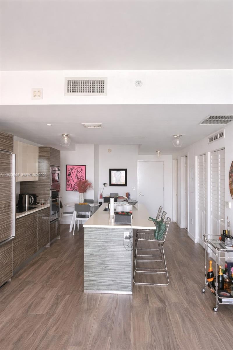 A modern kitchen features wood-grain cabinetry, a central island with bar seating, and light flooring — 460 NE 28th St # 2807, Miami FL 33137, MIAMI, FL