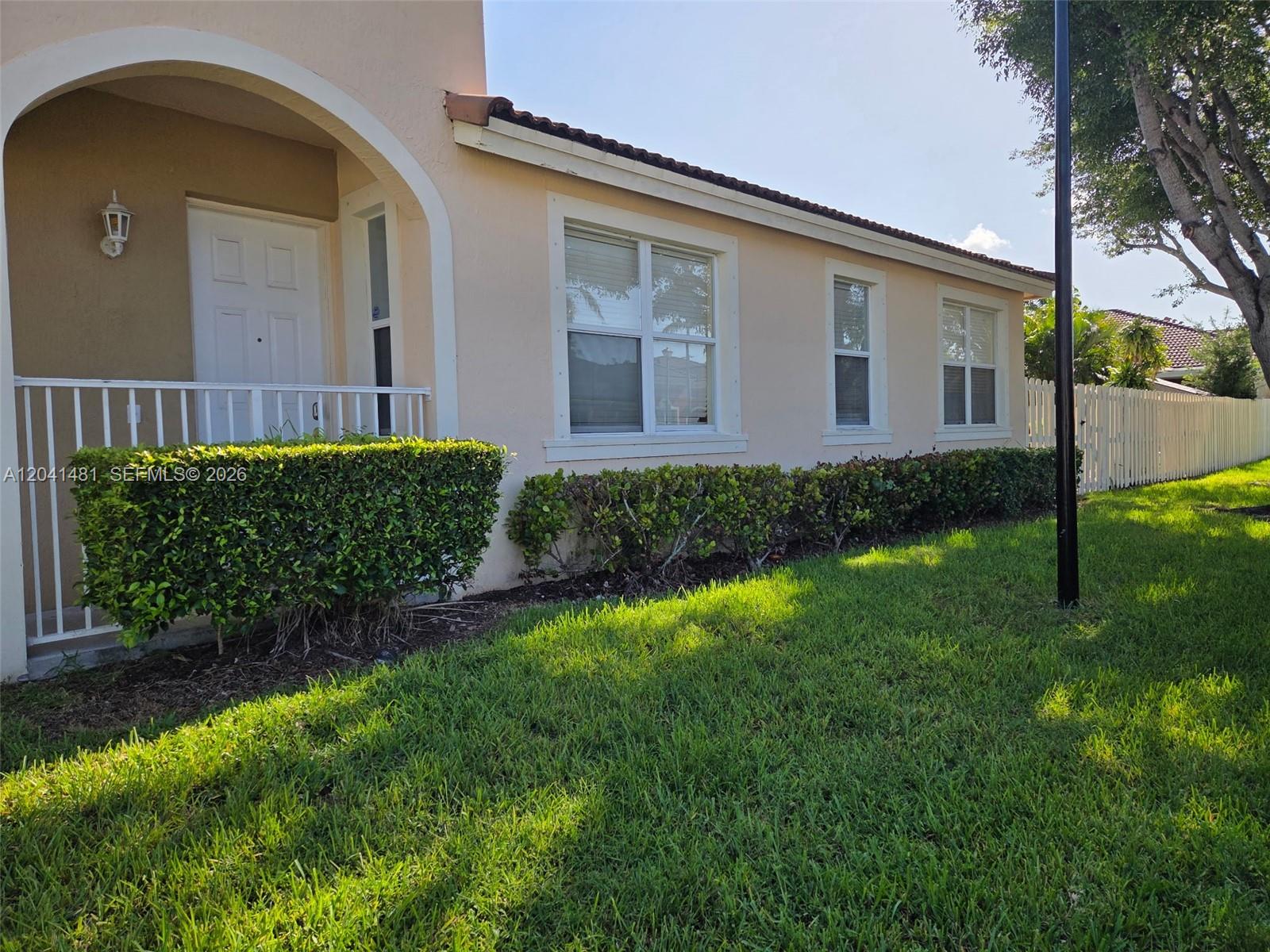 The exterior of a beige house features a covered entryway, white railings, and manicured hedges — 23751 SW 110th Ave, Homestead FL 33032, HOMESTEAD, FL