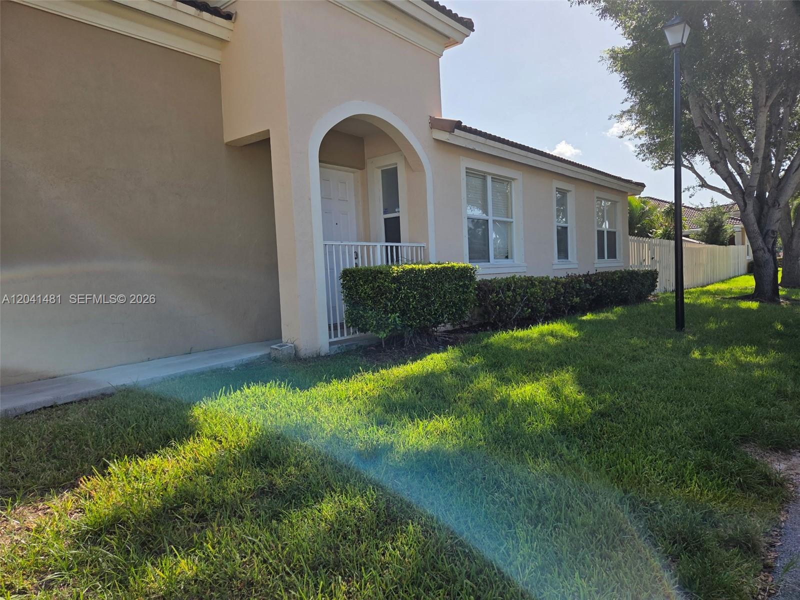 A tan stucco house features an arched entryway, white trim, and a manicured lawn — 23751 SW 110th Ave, Homestead FL 33032, HOMESTEAD, FL