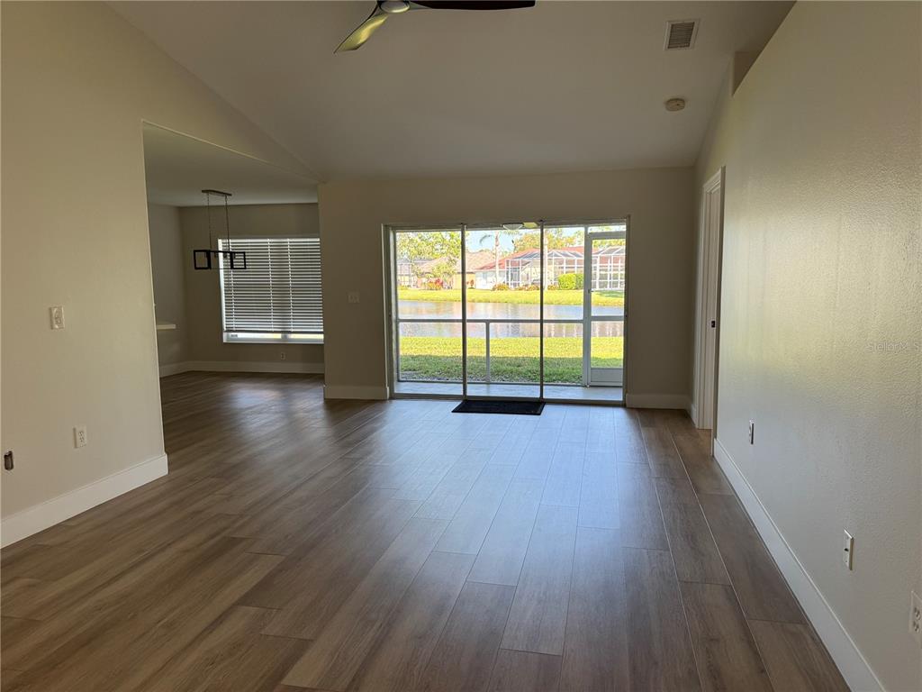 An open living area with wood-look tile flooring, vaulted ceilings, and a sliding door to a lake — 3709 62ND AVENUE E, BRADENTON, FL