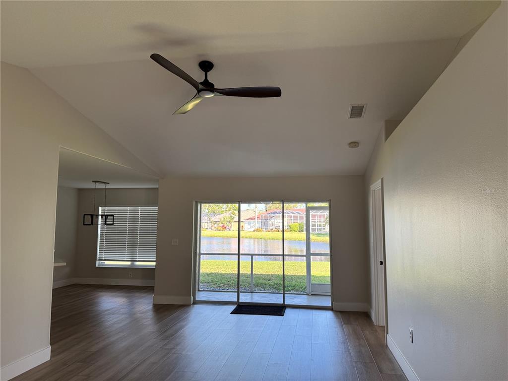A living room with wood-look tile flooring, a ceiling fan, and sliding doors to a lake — 3709 62ND AVENUE E, BRADENTON, FL