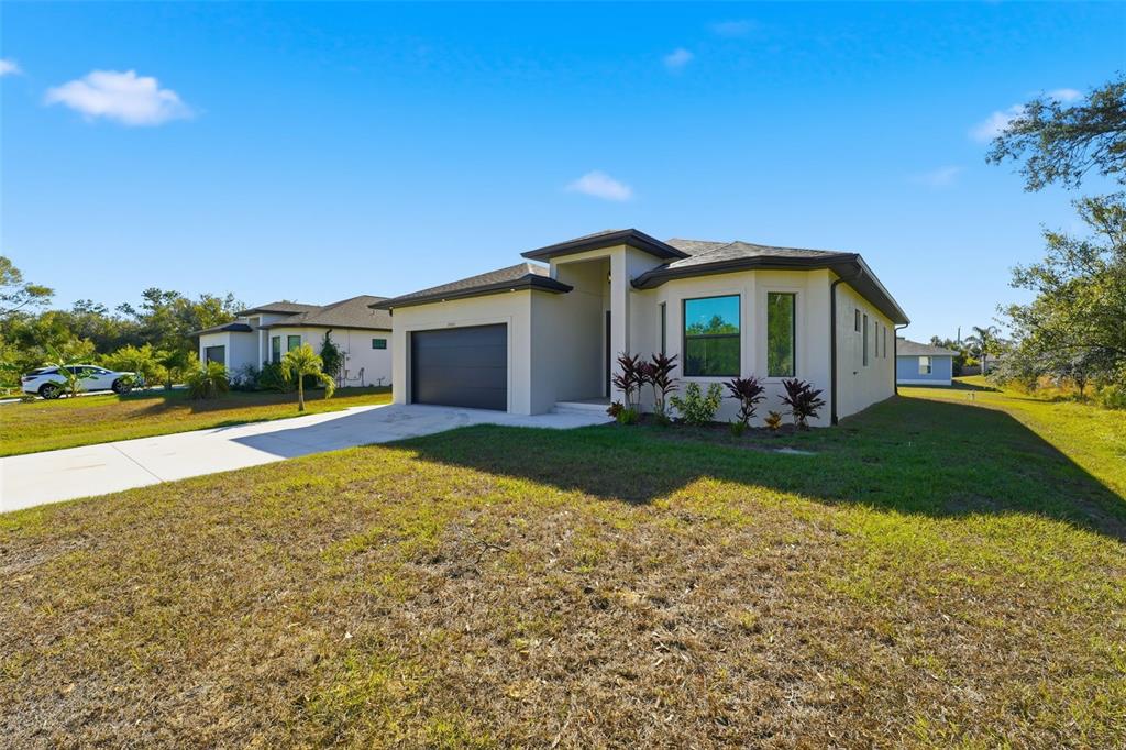 A modern, single-story suburban house with a garage, concrete driveway, and landscaped front yard — 12005 CARNIVAL AVENUE, PORT CHARLOTTE, FL