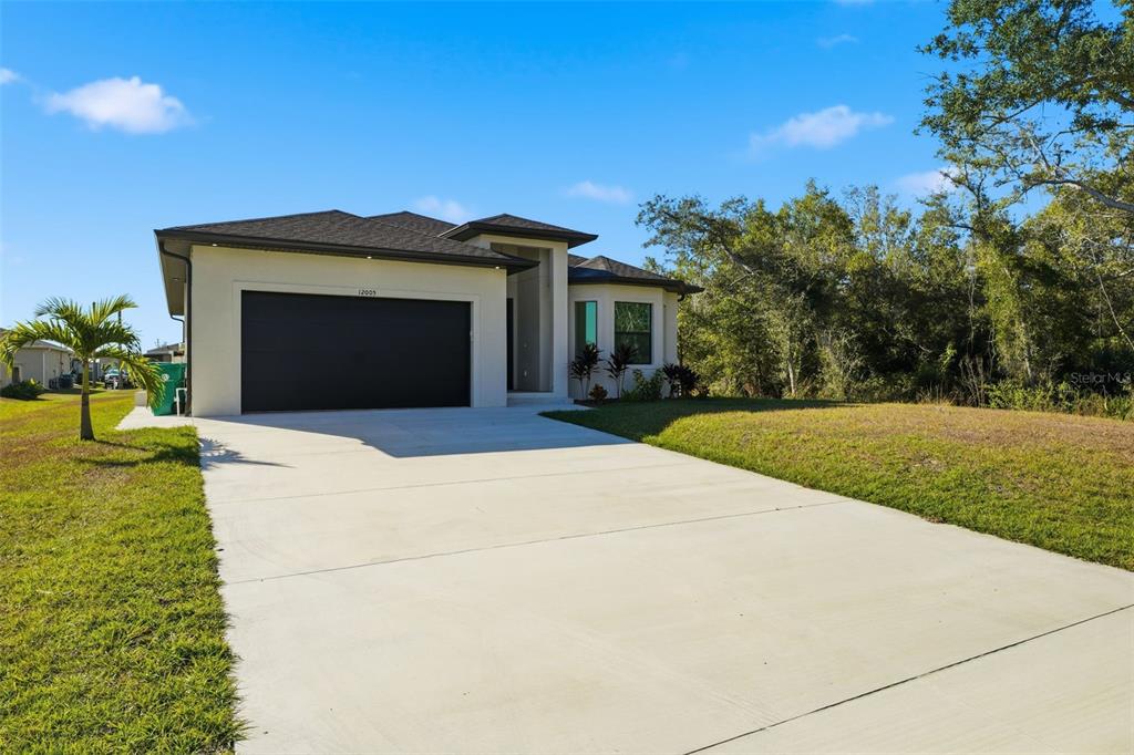A single-story house with a black garage door and a concrete driveway under a blue sky — 12005 CARNIVAL AVENUE, PORT CHARLOTTE, FL
