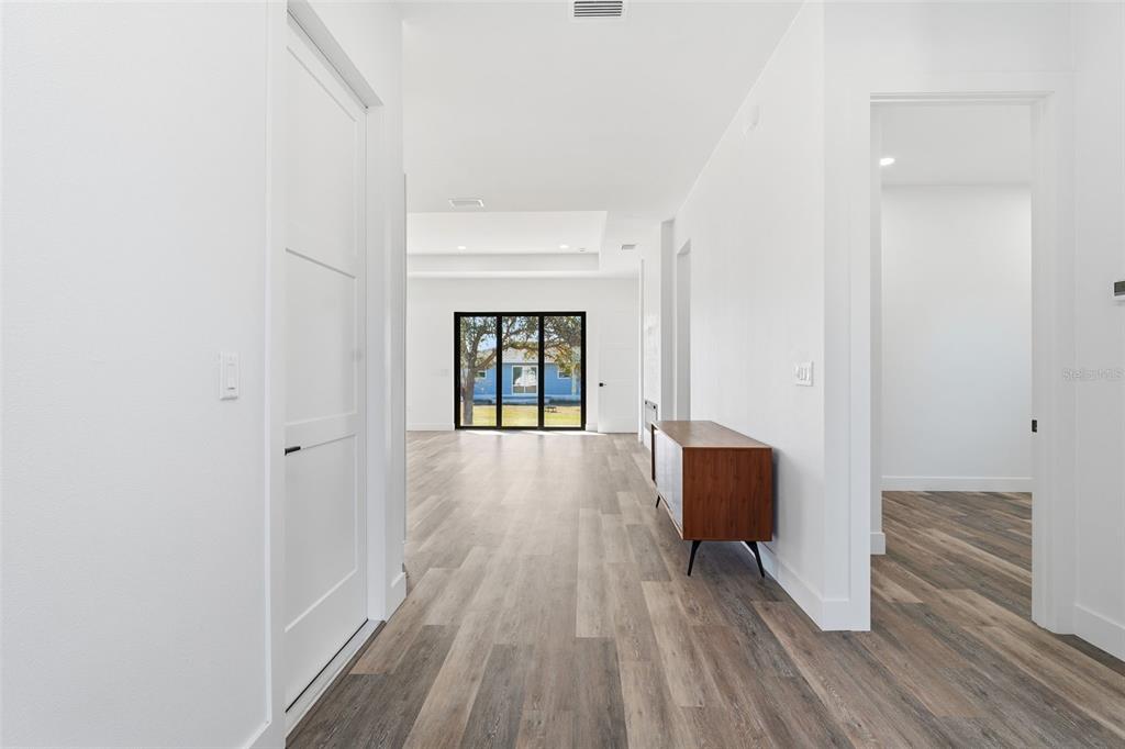A bright hallway with wood-look flooring leads toward a living area with large glass doors — 12005 CARNIVAL AVENUE, PORT CHARLOTTE, FL
